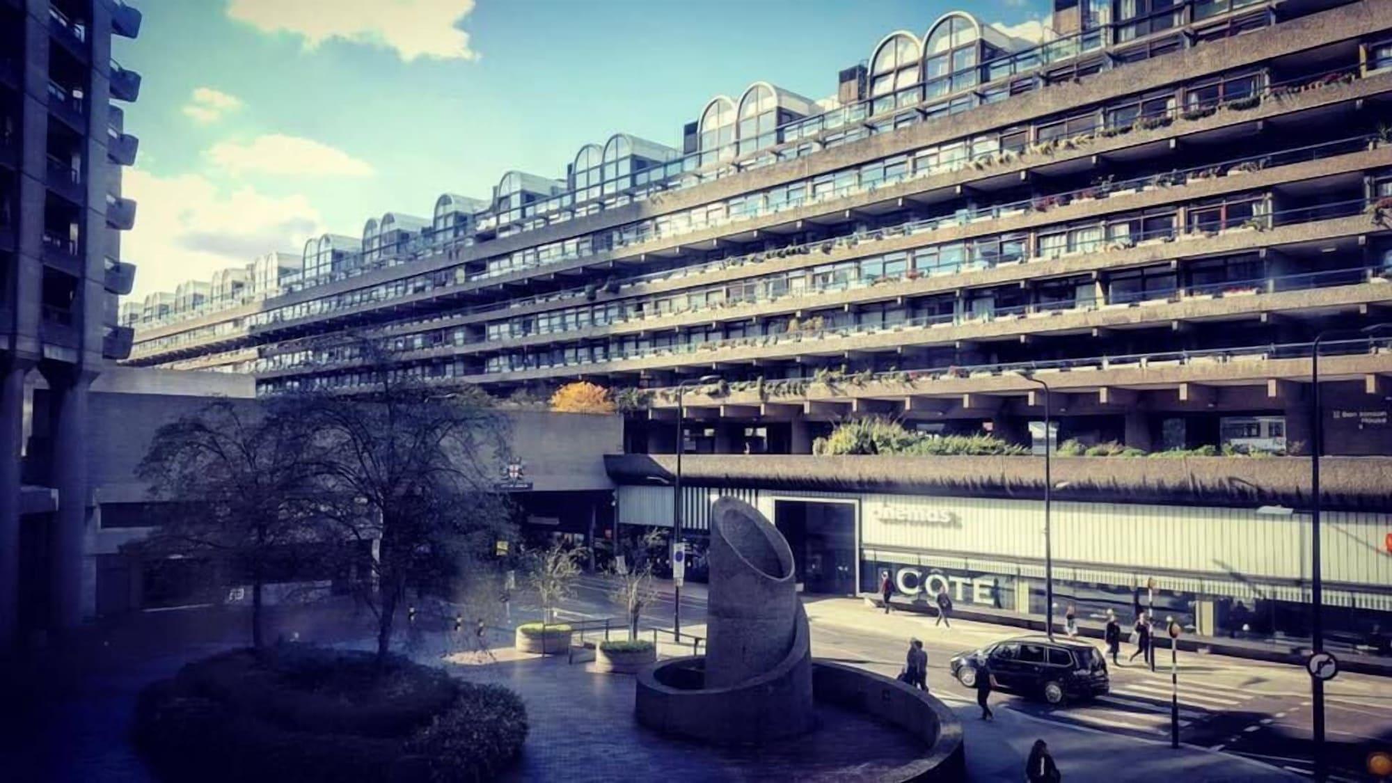 Montcalm Brewery Townhouse Hotel Londres Exterior foto The photo shows a modern architectural structure with multiple levels, featuring a series of large, rectangular balconies. Below this building, there is a plaza or courtyard area with a sculptural piece, which appears to be made of stone. Surrounding