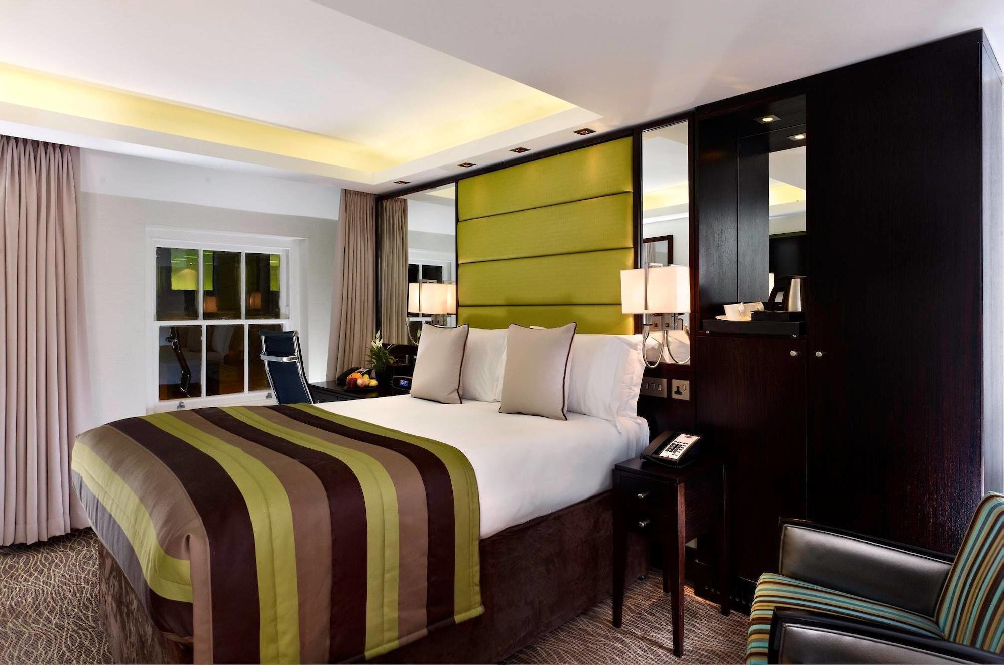 Montcalm Brewery Townhouse Hotel Londres Exterior foto The photo shows a modern hotel room featuring a large bed with a striped comforter in shades of green, brown, and cream. The bed is adorned with several decorative pillows. Behind the bed, there is a contemporary headboard with a green panel design. 