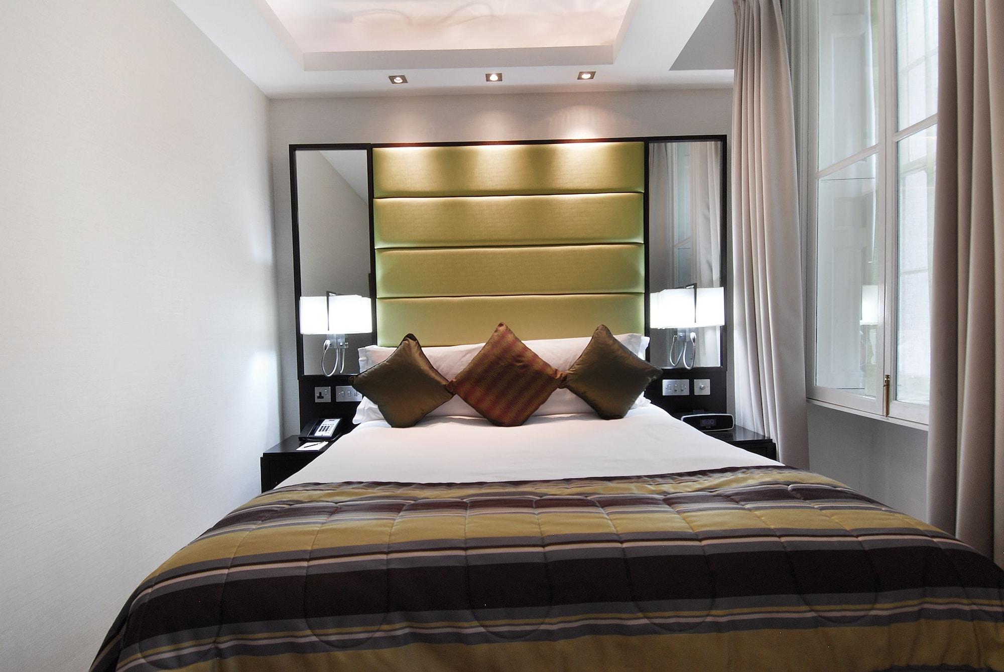 Montcalm Brewery Townhouse Hotel Londres Exterior foto The photo shows a stylishly decorated bedroom. The bed is centered in the room, featuring a white comforter with a plaid pattern in shades of brown and green. There are three decorative pillows on the bed, two in shades of brown and one in dark green