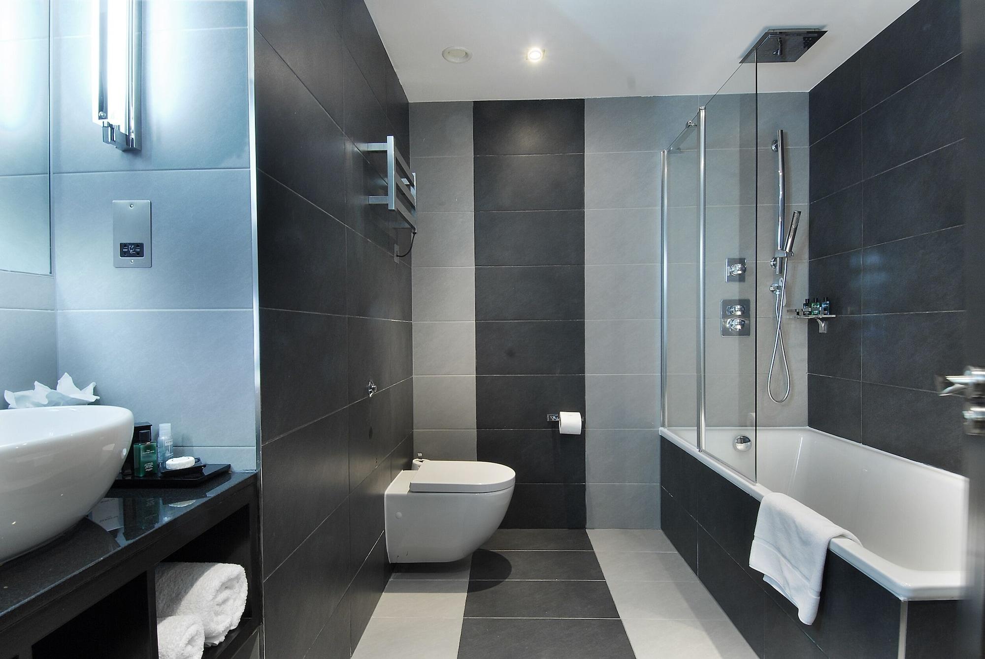 Montcalm Brewery Townhouse Hotel Londres Exterior foto The photo shows a modern bathroom featuring a sleek design. The walls are tiled in a combination of dark gray and light gray, creating a contemporary look. On the left, there is a countertop with a basin and some toiletries placed on it. The middle s
