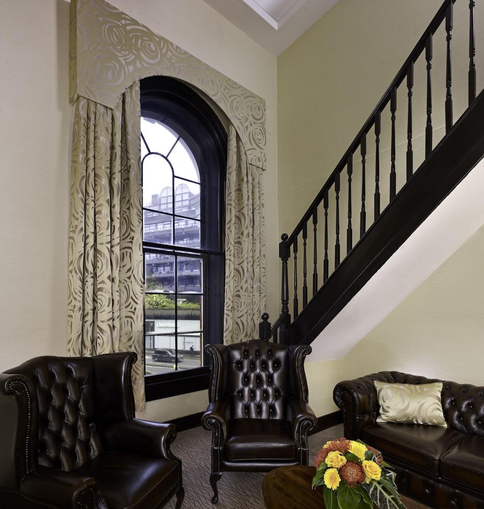 Montcalm Brewery Townhouse Hotel Londres Exterior foto The photo shows a cozy interior space featuring two elegant leather armchairs placed near a large, ornate window with arched top and decorative curtains. The wall is painted in a muted color, enhancing the warmth of the room. A staircase with black s