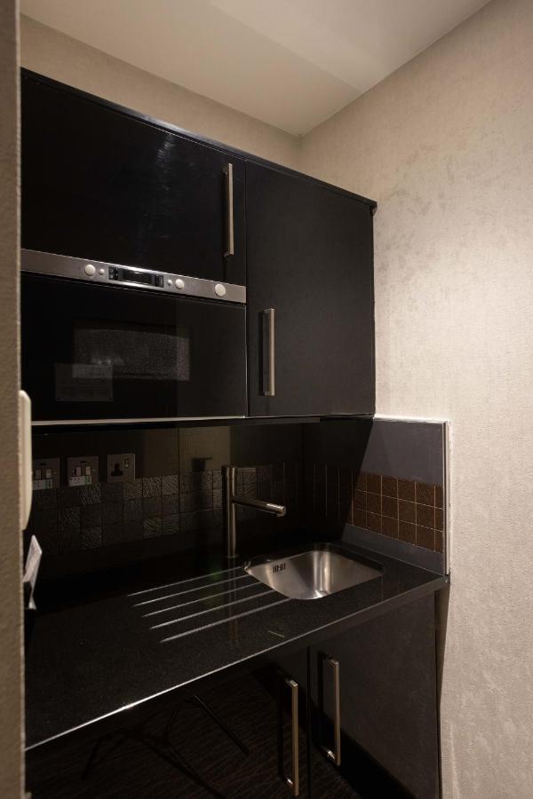 Montcalm Brewery Townhouse Hotel Londres Exterior foto The photo shows a modern kitchen setup with a dark color scheme. It features:

- A built-in microwave oven situated above a countertop.
- A sleek black cabinet beneath the microwave, which likely stores kitchen items.
- A stainless steel sink placed 