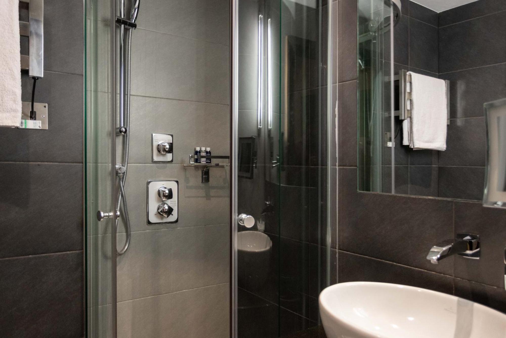 Montcalm Brewery Townhouse Hotel Londres Exterior foto The photo shows a modern bathroom with a glass shower enclosure. The shower features a handheld showerhead and various controls mounted on the wall. The walls are tiled in dark, sleek tones, contributing to a contemporary aesthetic. There is a round 