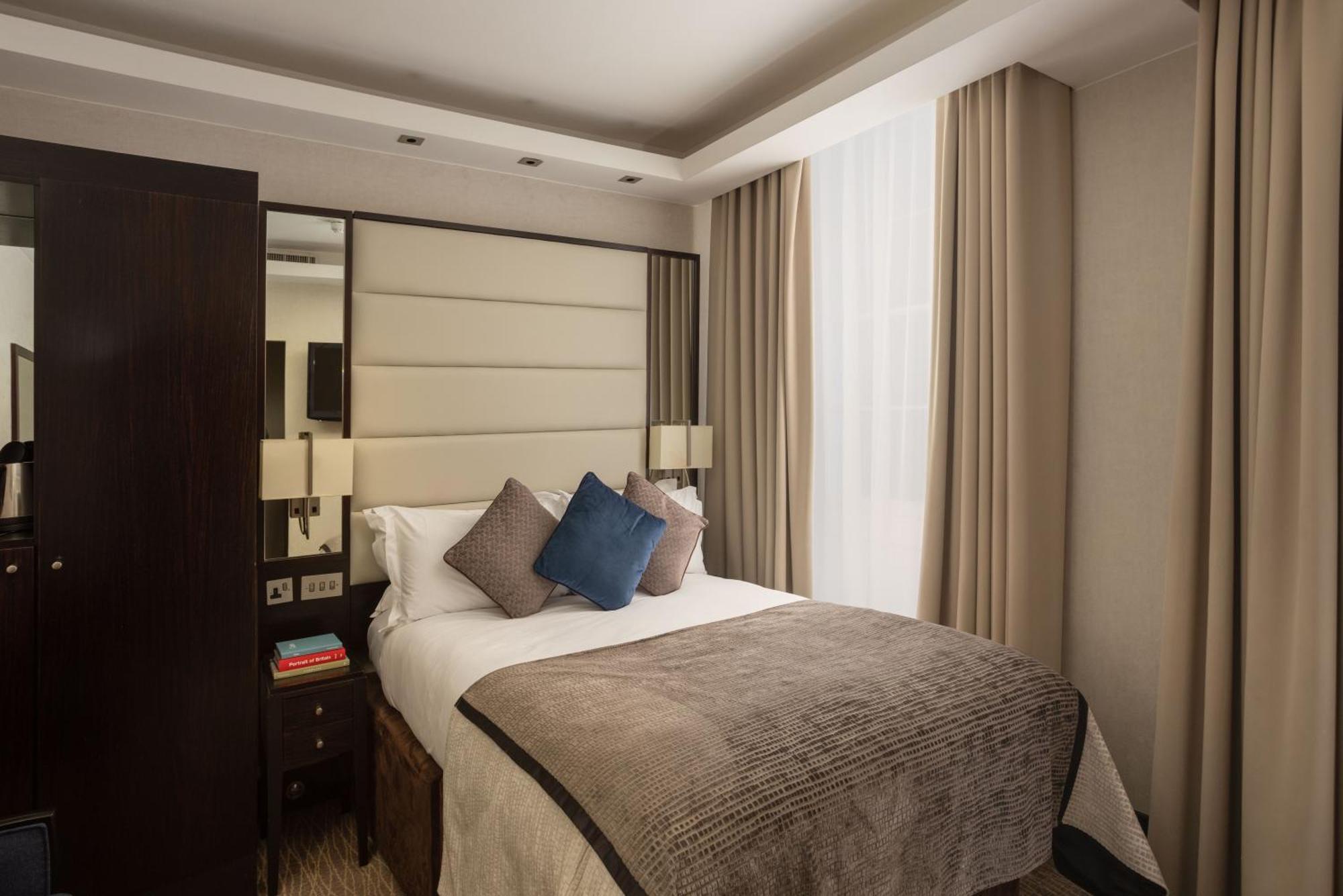 Montcalm Brewery Townhouse Hotel Londres Exterior foto The photo shows a modern hotel room with a cozy design. It features a double bed with a light-colored headboard and a soft, stylish blanket. There are decorative pillows on the bed, including a blue one. On either side of the bed, there are small nig