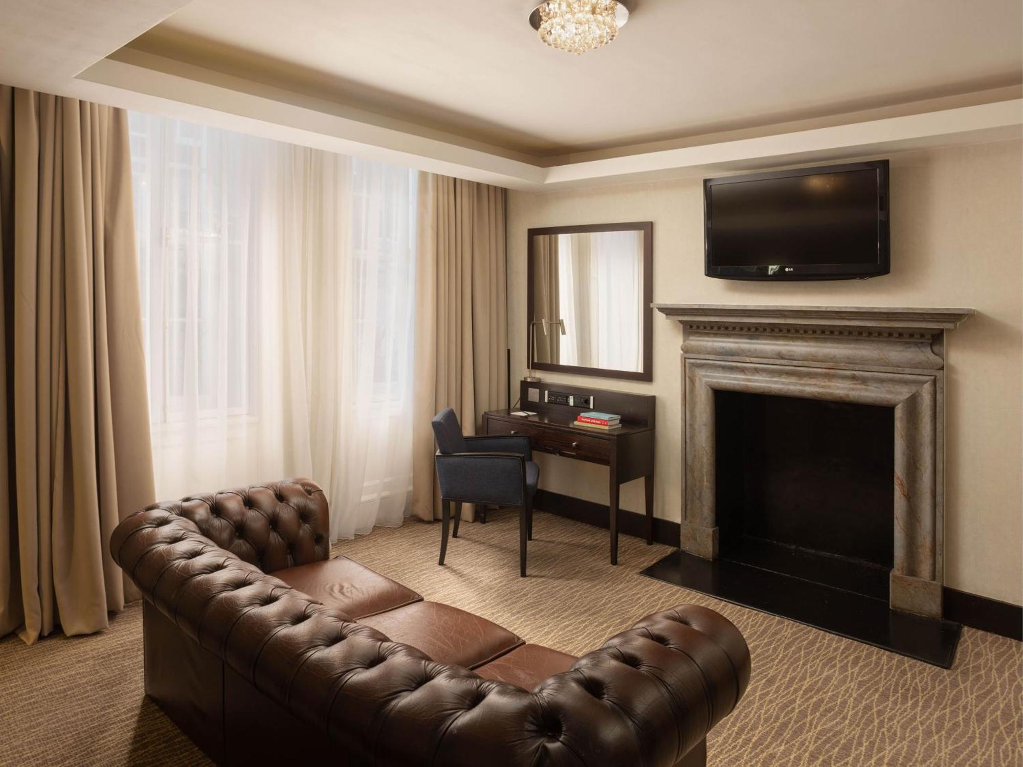 Montcalm Brewery Townhouse Hotel Londres Exterior foto The photo shows a cozy and elegantly designed room. There is a comfortable brown leather sofa with tufted detailing. A small desk and chair are positioned near a mirror, providing a space for work or personal grooming. On the wall, a flat-screen TV i