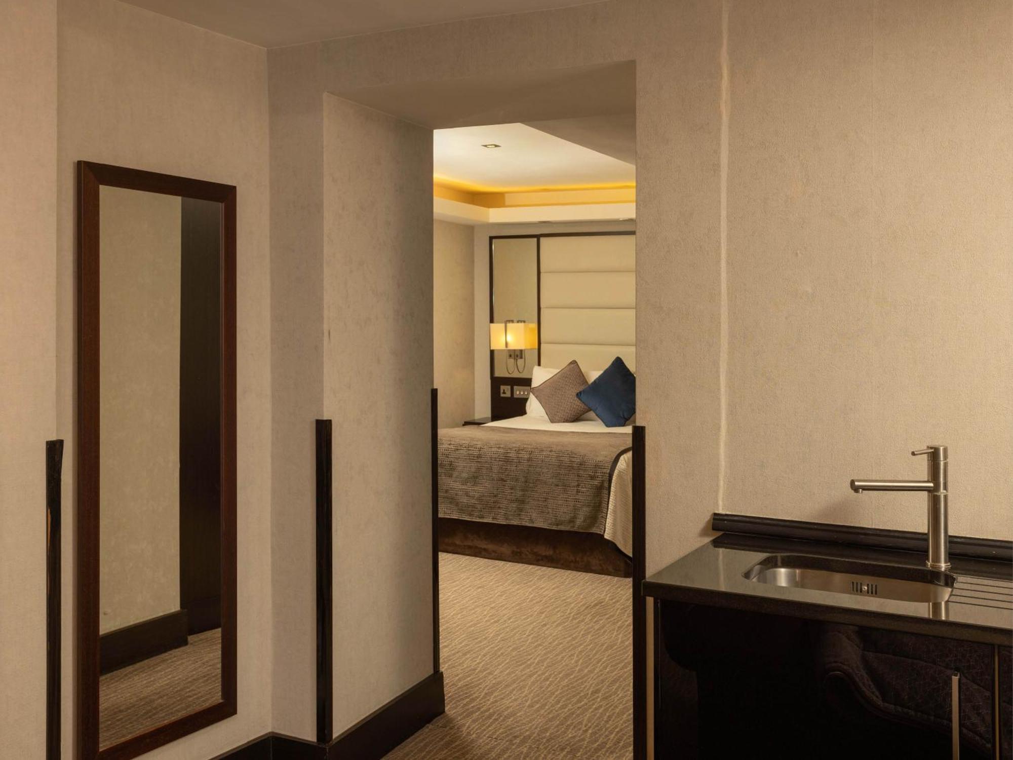 Montcalm Brewery Townhouse Hotel Londres Exterior foto The photo shows an interior space that appears to be a hotel room or a suite. There is a doorway leading to a bedroom visible in the background, where a bed with decorative pillows can be seen. To the side, there is a small wet bar or kitchenette are