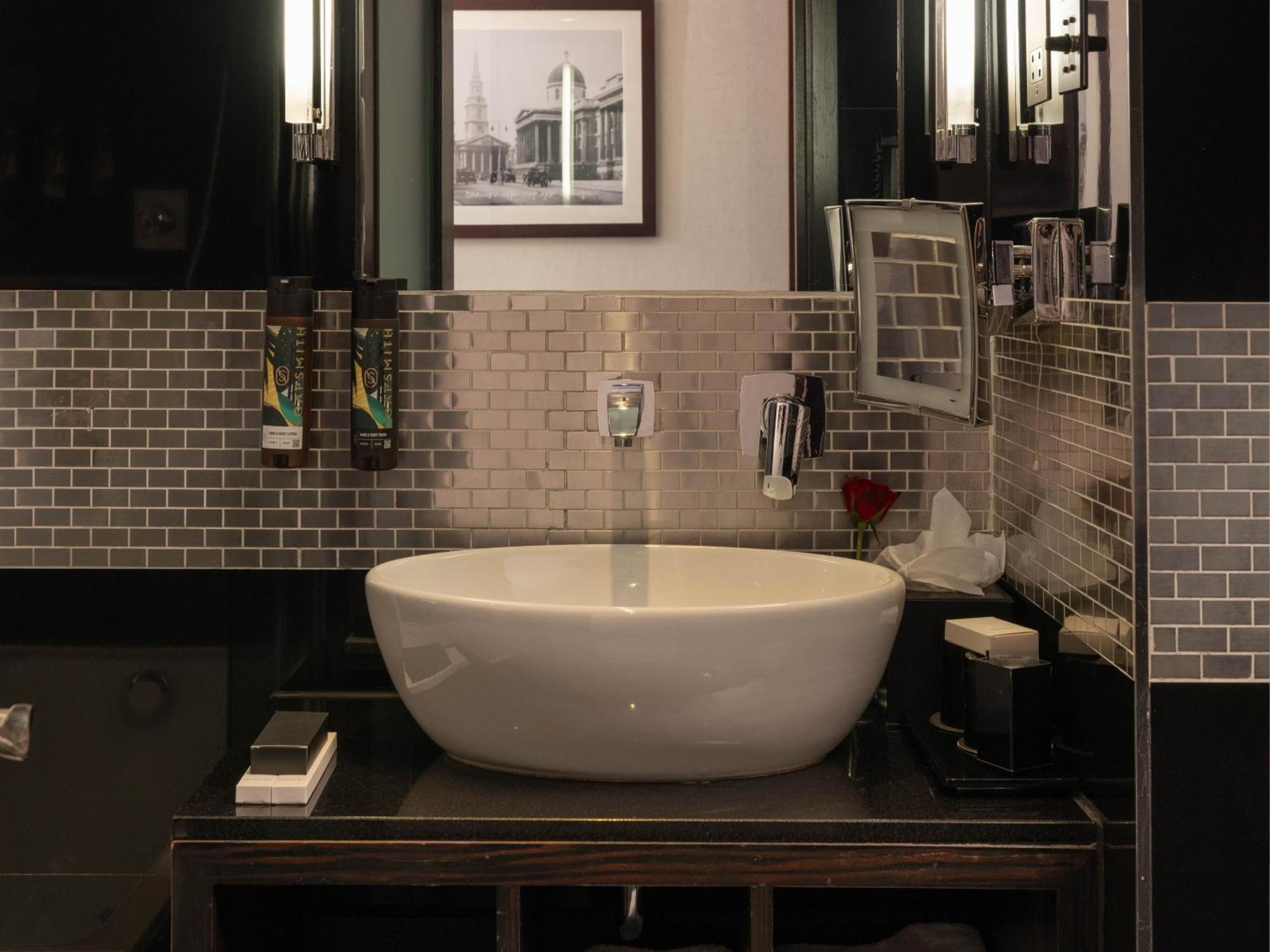 Montcalm Brewery Townhouse Hotel Londres Exterior foto The photo shows a modern bathroom with a stylish design. It features a large, round white sink placed on a dark wooden vanity. The walls are adorned with a mix of gray and silver tile, creating a sleek and contemporary look. Above the sink, there is 