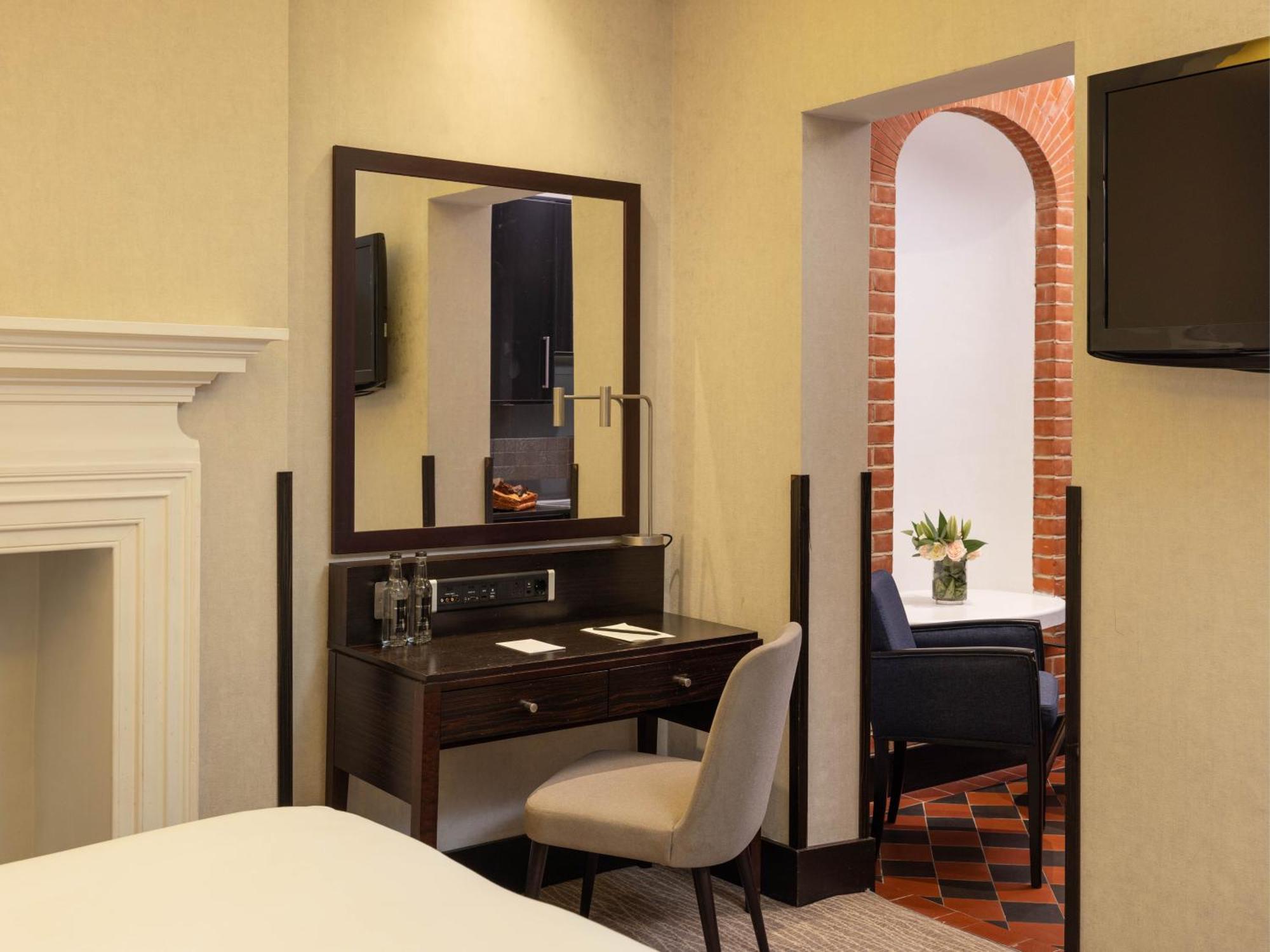 Montcalm Brewery Townhouse Hotel Londres Exterior foto The photo displays a hotel room setup. On the left side, there's a bed with a simple white bedding arrangement. Adjacent to the bed, there's a wooden desk with a chair, along with a mirror above the desk. The desk area is equipped with some glassware