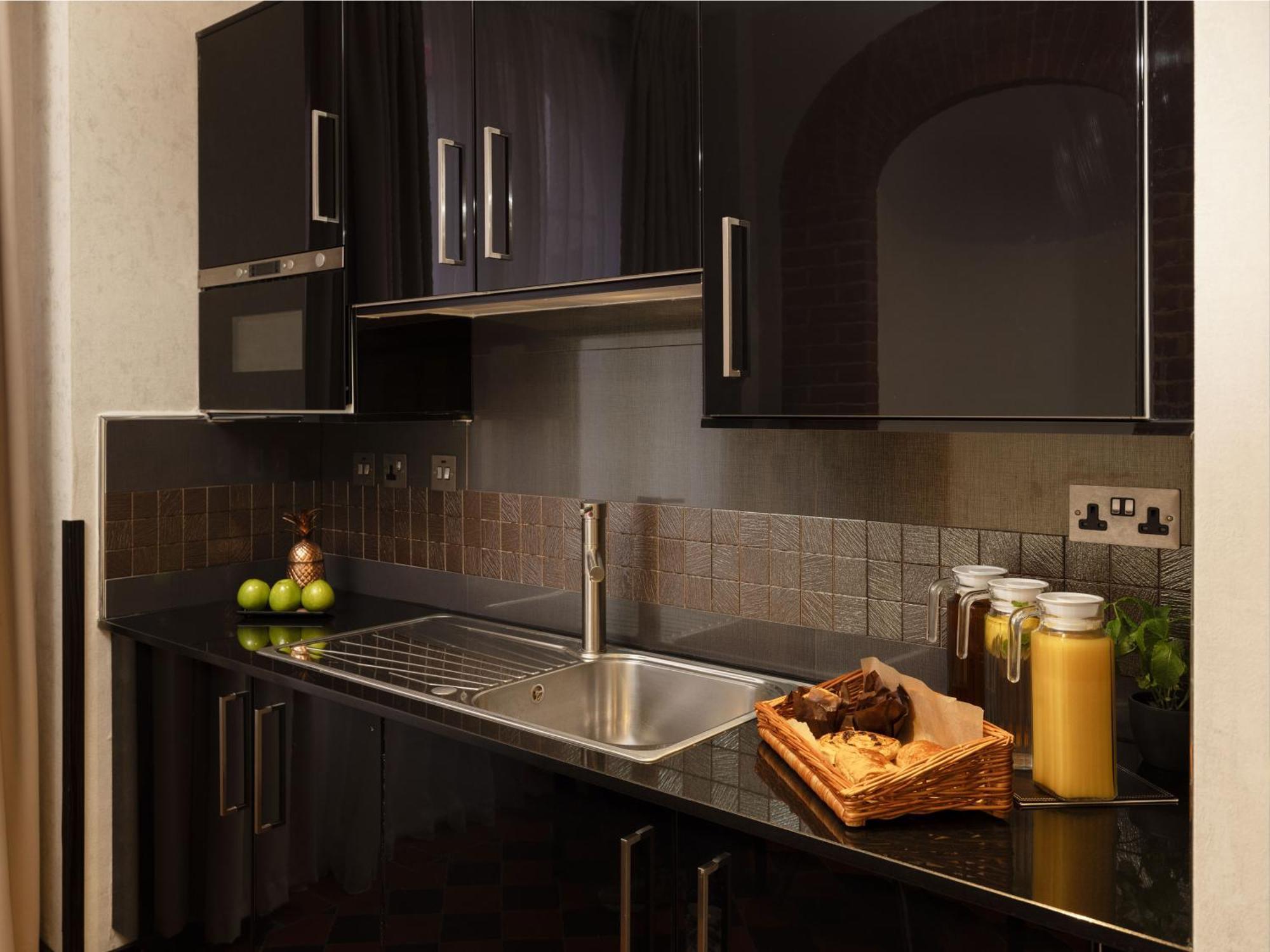 Montcalm Brewery Townhouse Hotel Londres Exterior foto The photo shows a modern kitchen with sleek black cabinetry and a glossy finish. The kitchen features a stainless steel sink with a contemporary faucet, set against a dark, textured countertop. Above the counter, there are cabinets that match the cou