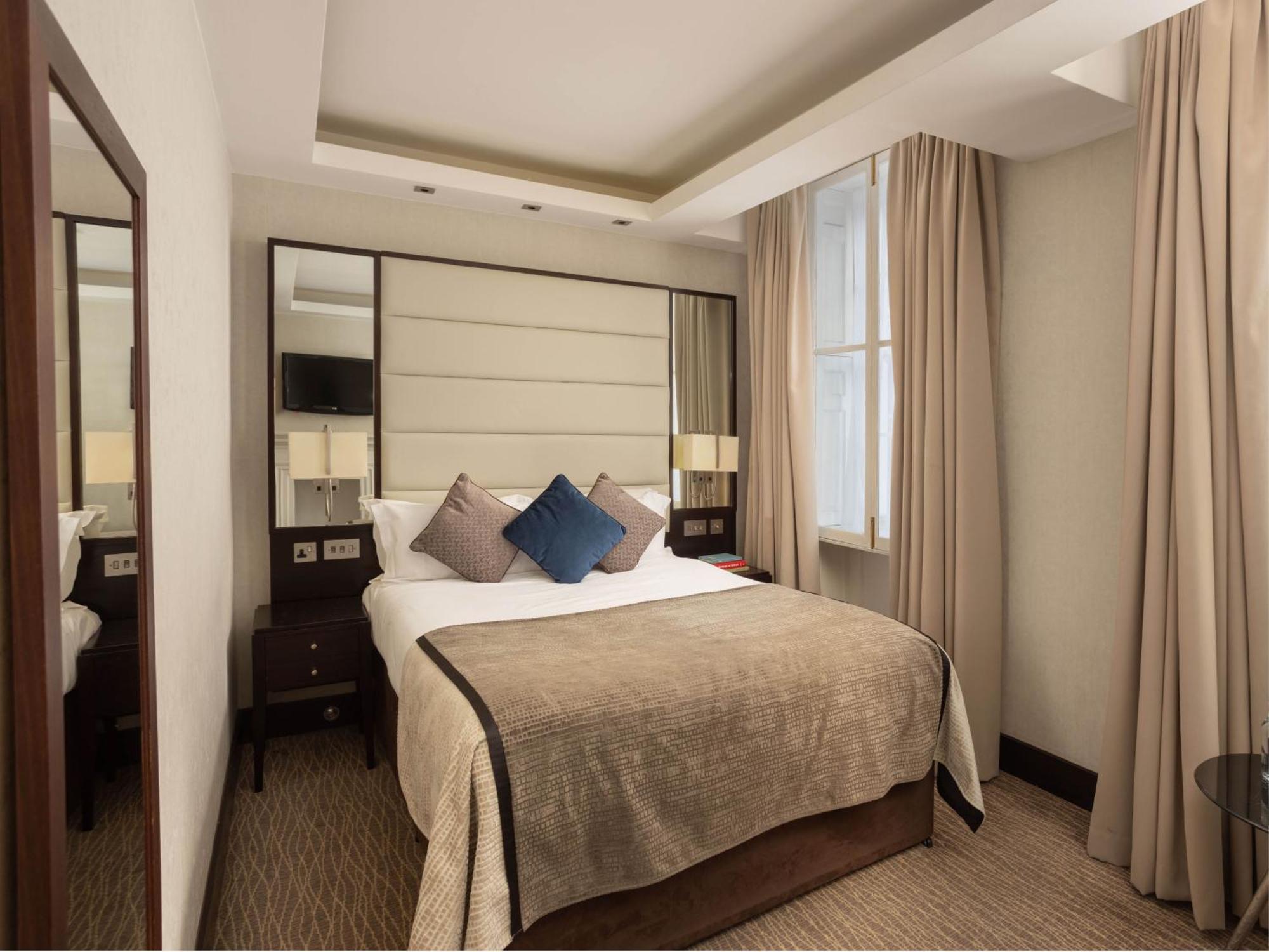Montcalm Brewery Townhouse Hotel Londres Exterior foto The photo shows a cozy hotel room with a bed as the focal point. The bed is made with neutral-colored linens and has several pillows, including a decorative blue one. There are bedside tables on either side of the bed, each with a lamp. A large mirro