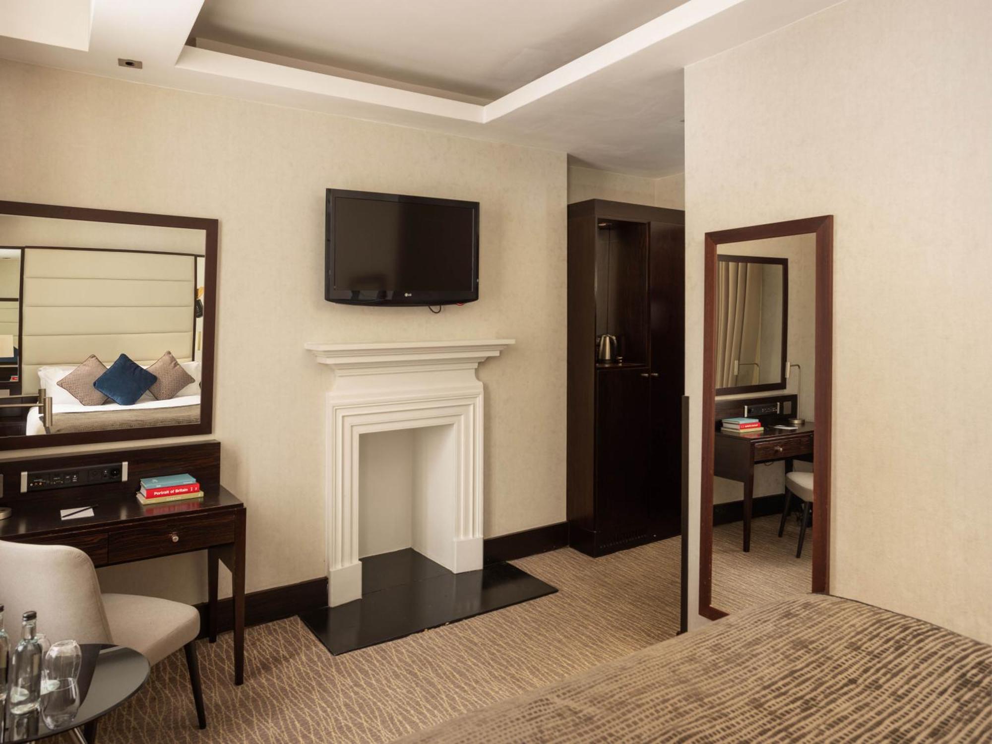 Montcalm Brewery Townhouse Hotel Londres Exterior foto The photo depicts a stylish hotel room. It features a double bed, a large flat-screen TV mounted on the wall, and a decorative fireplace. There is a wooden desk with a chair beside it, as well as a mirror hanging on the wall. The decor is modern and 