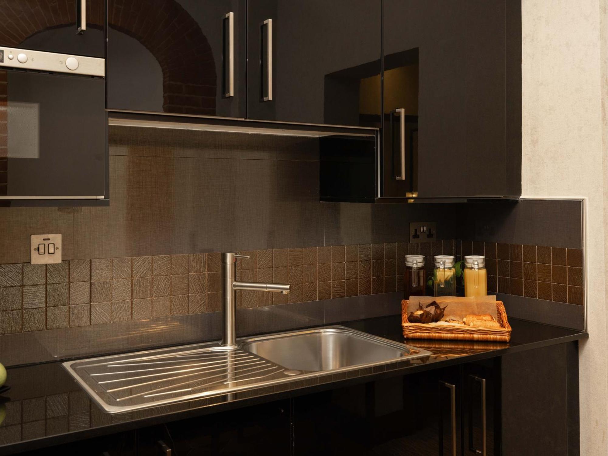 Montcalm Brewery Townhouse Hotel Londres Exterior foto The photo shows a modern kitchen with a sleek design. It features dark cabinetry with a glossy finish and stainless steel handles. There is a stainless steel sink with a simple faucet, and a countertop made of black material. Above the sink, there ar