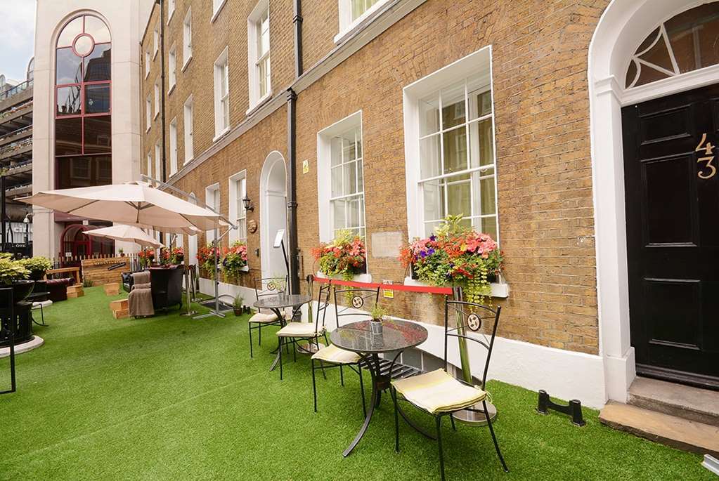 Montcalm Brewery Townhouse Hotel Londres Exterior foto The photo depicts a charming outdoor area in front of a building with a warm, textured brick facade. There is a neatly maintained lawn, likely made of artificial grass, and several small round tables with chairs are arranged outside. Flower pots with