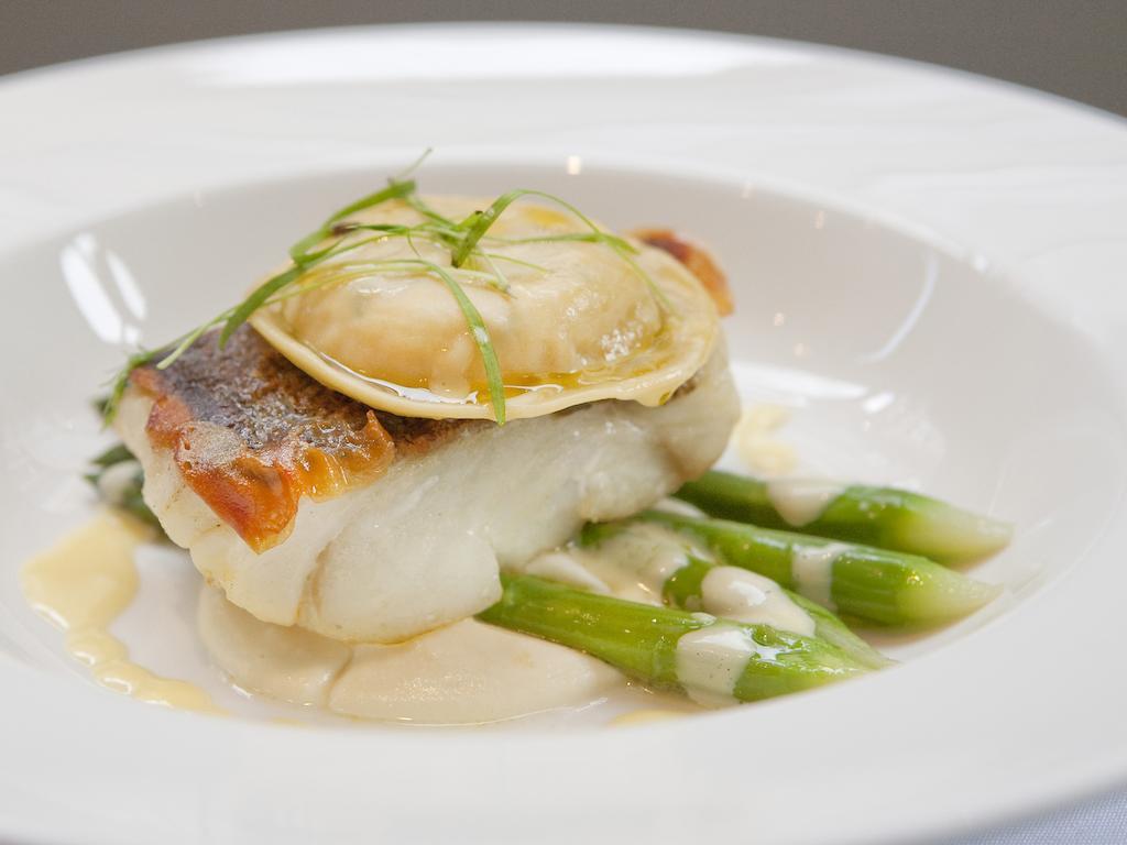 Montcalm Brewery Townhouse Hotel Londres Exterior foto The image shows a beautifully presented dish featuring a piece of fish, likely a white fish, topped with a clam. It is served on a bed of green asparagus spears. The dish is garnished with thinly sliced herbs or greens, adding a touch of color. The s