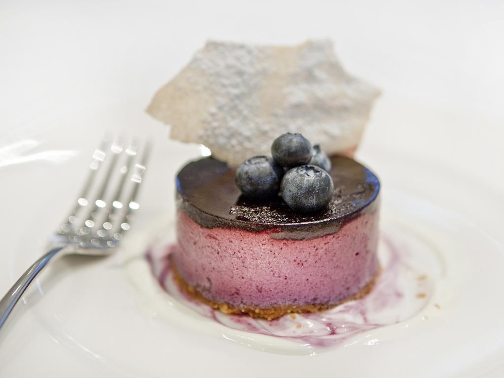 Montcalm Brewery Townhouse Hotel Londres Exterior foto The photo shows a beautifully plated dessert, which appears to be a round cheesecake or mousse. It has a pinkish-purple filling, topped with a glossy dark chocolate layer. Three fresh blueberries sit on top, adding a pop of color. The dessert is acco