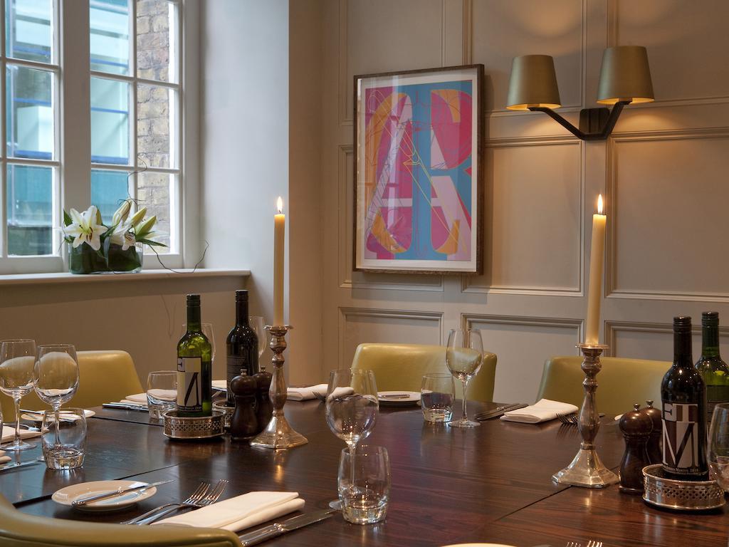 Montcalm Brewery Townhouse Hotel Londres Exterior foto The photo shows an elegantly set dining room with a large wooden table surrounded by several chairs. The table is adorned with neatly arranged utensils, glasses, and decorative items. There are two tall candlesticks with candles and several bottles o
