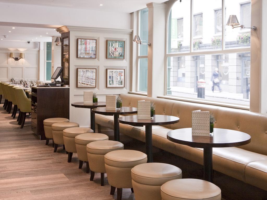 Montcalm Brewery Townhouse Hotel Londres Exterior foto The photo displays a modern café or restaurant interior. There is a cozy seating area featuring light-colored, upholstered benches along the wall, accompanied by small round tables. The tables are paired with circular stools. The decor includes frame