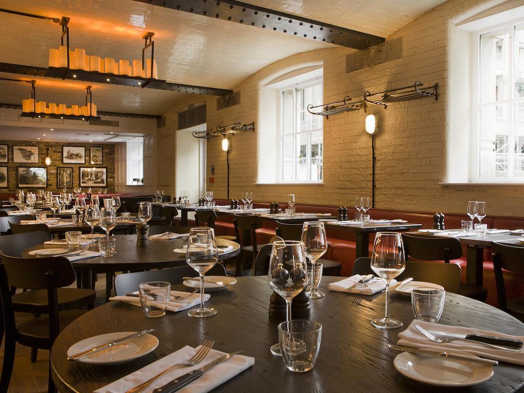 Montcalm Brewery Townhouse Hotel Londres Exterior foto The photo shows a restaurant interior featuring a warm and inviting atmosphere. It has several round wooden tables set for dining, each with neatly arranged plates, utensils, and glasses. The lighting is soft, with overhead fixtures providing a cozy 