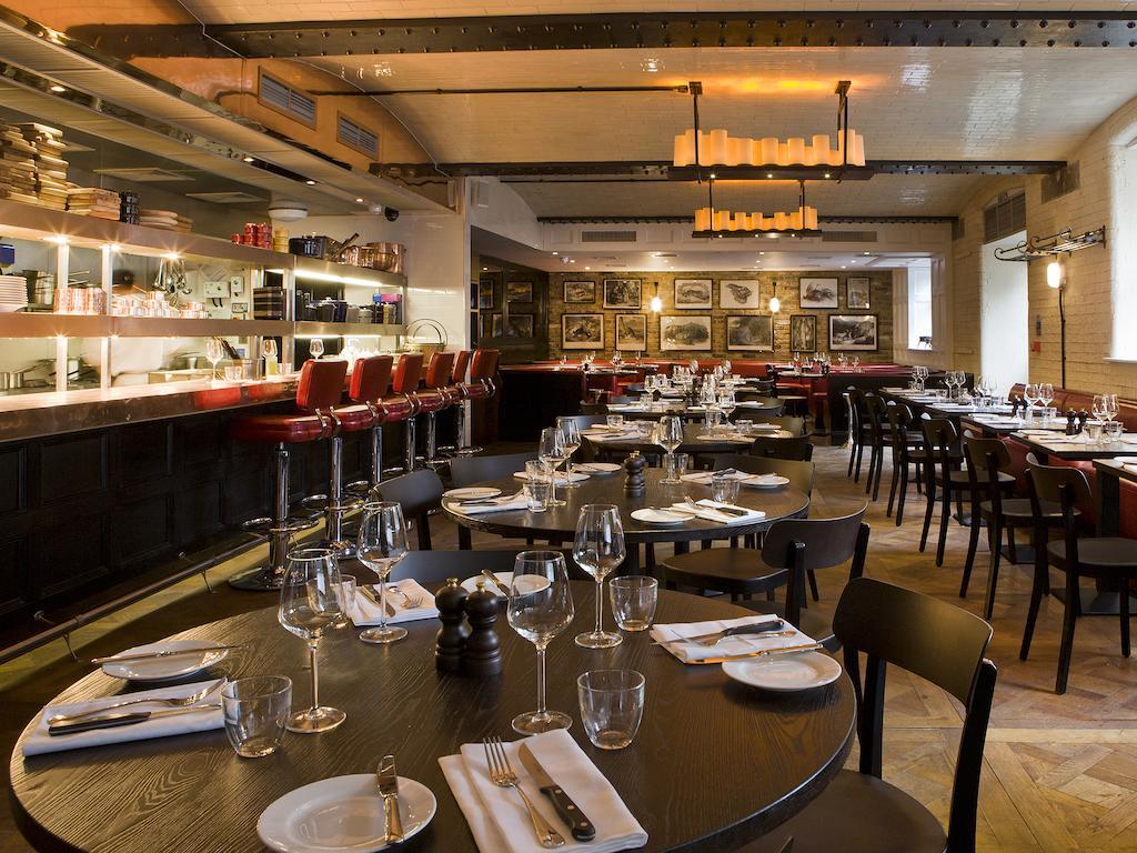 Montcalm Brewery Townhouse Hotel Londres Exterior foto The photo shows the interior of a stylish restaurant. It features several round tables set with white plates, glasses, and silverware, all neatly arranged for dining. The decor includes a modern design with wooden floors and a mix of lighting fixture