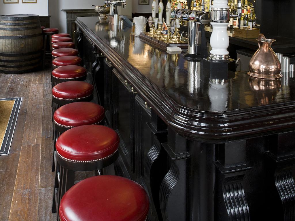 Montcalm Brewery Townhouse Hotel Londres Exterior foto The photo shows a bar setting with a long, polished dark wooden bar counter. Attached to the counter are several bar stools with red leather seats. Behind the bar, there are various bottles, suggesting a well-stocked bar. The flooring appears to be w