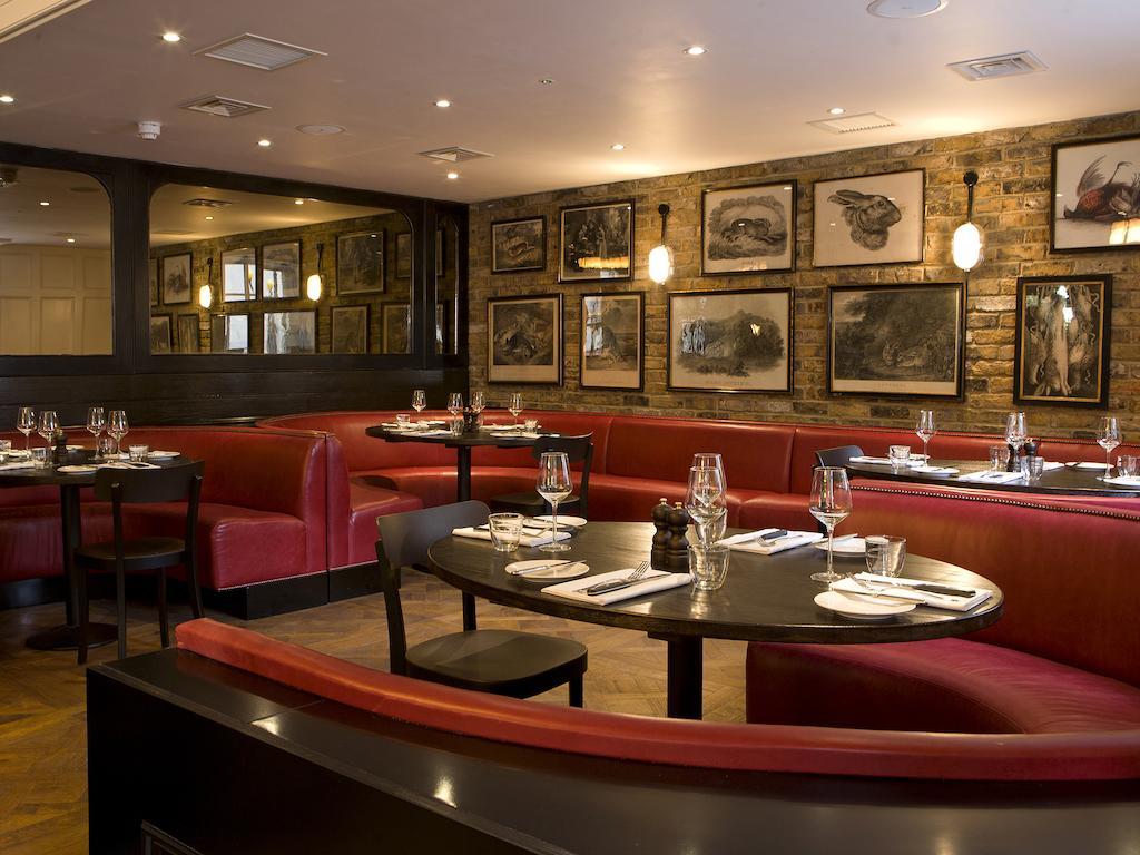 Montcalm Brewery Townhouse Hotel Londres Exterior foto The photo depicts an elegant restaurant interior. There are curved red booths along the walls, creating a cozy seating arrangement. The tables are round and set with white plates and glassware, indicating a prepared dining area. The walls feature a n
