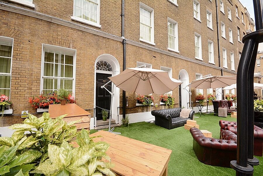 Montcalm Brewery Townhouse Hotel Londres Exterior foto The photo depicts an outdoor area of a building with a brick facade. There are several large windows visible, along with a wooden door. The setting features outdoor furniture, including couches in a dark leather finish and wooden tables. Large umbrel